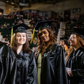 Two graduates smile for the camera as they enter Commencement 2025