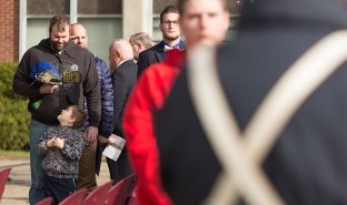 A young boy looks up at his man while saluting during a Veterans Day ceremony on campus