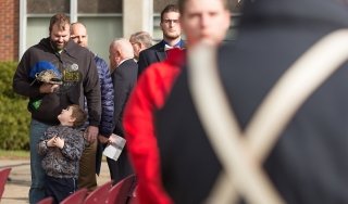 A young boy looks up at his man while saluting during a Veterans Day ceremony on campus