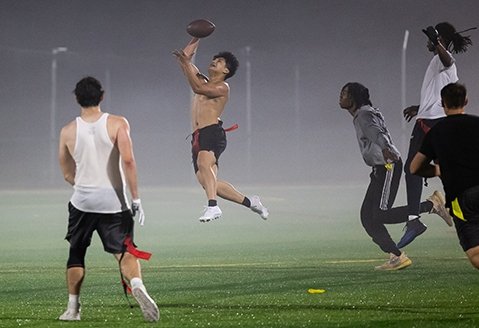 A group of students play football on the turf field under the lights