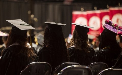 Four graduates are seen from behind, sitting in Harding Mazzotti Arena, at Commencement 2026
